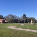 Photo of an open grass area with winding gravel path running though it and a children's play area and housing in the background