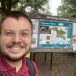 Photo of a warden, smiling, standing in front of the Whitmoor Common noticeboard at Salt Box Road.