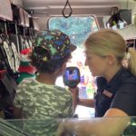 Photo of a little child inside a fire engine, holding up a piece of hand held equipment.