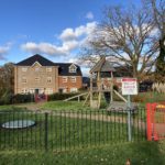 Photo of a children's play area enclosed by black metal fencing, with houses behind