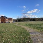 Photo of an open grassy area with a surfaced path winding through it and houses in the background